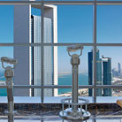 Interior view of the Etihad Towers observation deck in Abu Dhabi, UAE, showcasing binoculars and the panoramic cityscape.