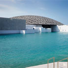 Exterior view of the Louvre Museum Abu Dhabi from a different angle, showcasing its iconic dome structure reflecting in the Arabian Sea.