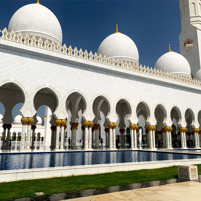 Exterior view of the Sheikh Zayed Grand Mosque in Abu Dhabi, showcasing its dazzling white facade, towering minarets, and intricate floral mosaics.