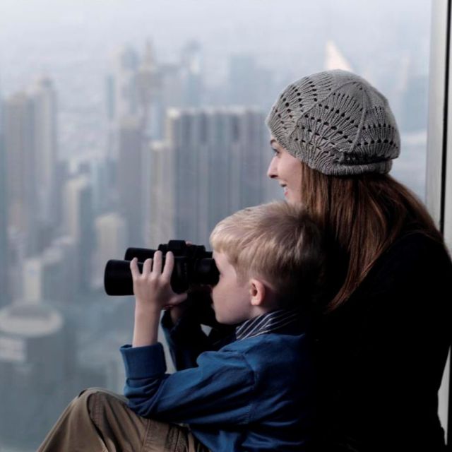 Mother and son enjoying panoramic view of Dubai City from Burj Khalifa observation deck, using binoculars