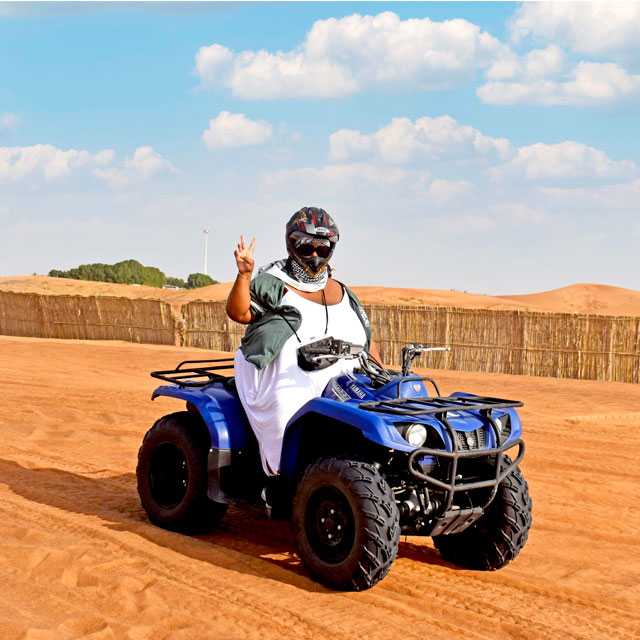 Woman celebrating with victory gesture while riding quad bike on Dune Rider Adventure in Dubai