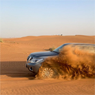Nissan Patrol 4x4 powers through a sand dune on a Dubai desert safari adventure. The entire left side of the vehicle is buried in sand, with only the front wheel and headlight visible.