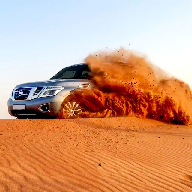  Nissan Patrol 4x4 tackling a sand dune on a Dubai desert safari. Sand covers most of the left side of the vehicle, with only the front windshield and bumper visible.
