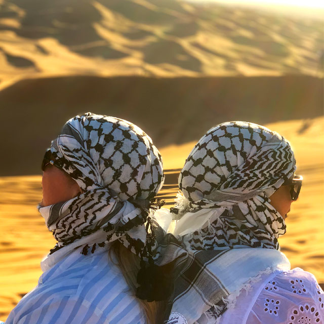 Two women posing on desert dunes during Prime Dubai Dunes Safari with dunes in the background.