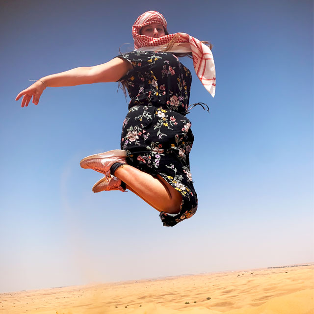 Thrilled woman in black dress enjoying Dubai dune bashing experience.