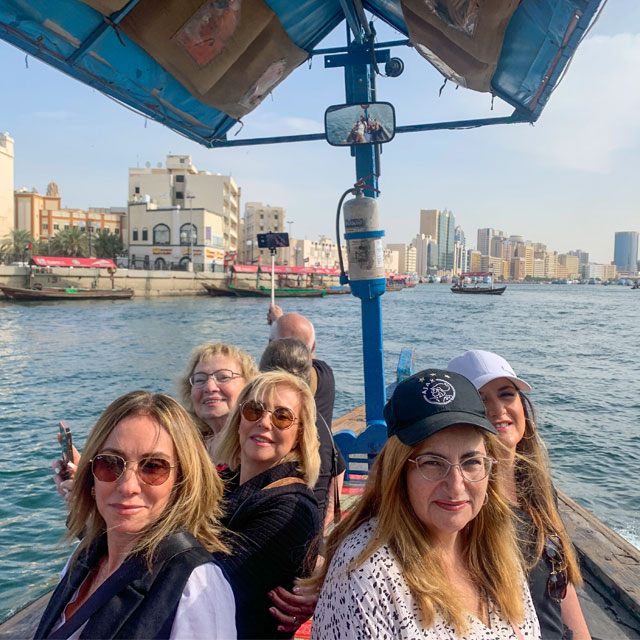 Tourists enjoying a traditional abra water taxi ride on Dubai Creek, capturing a close-up photo with the backdrop of Old Dubai and other sailing abras.