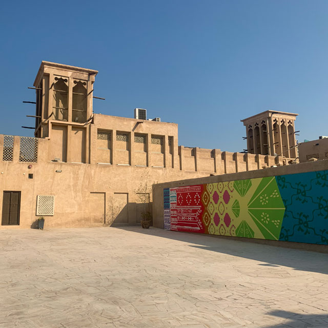 Al Fahidi Historical Neighbourhood in Dubai featuring a traditional wind tower and a colorful mural on a building facade.