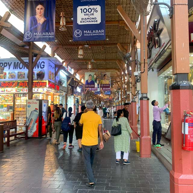 Entrance to the long walkway of Dubai's Old Gold Souk, featuring a banner for Malabar Jewellers hanging above the archway.